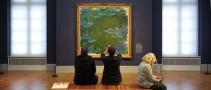 Besucher sitzen im Museum Barberini vor dem Bild „Seerosen“ (1914 bis 1917) von Claude Monet auf einer Bank.