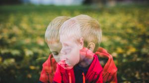 Ein Junge im Grundschulalter sitzt mit traurigem Blick auf einer Wiese.