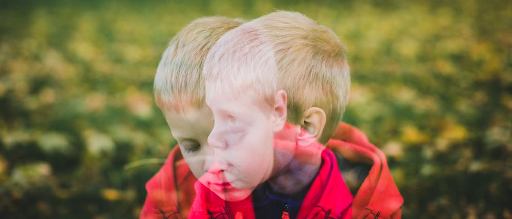 Ein Junge im Grundschulalter sitzt mit traurigem Blick auf einer Wiese.