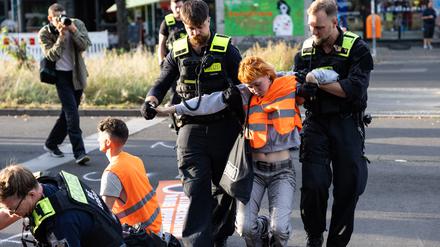 Eine Aktivistin wird von zwei Polizisten von der Straße getragen.