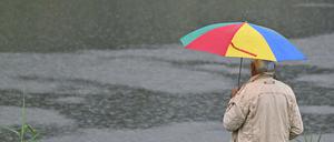 Ein Mann mit Regenschirm steht am Fluss Schwarze Elster. 