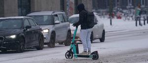Ein Mann fährt mit einem E-Scooter über eine verschneite Straße. (Symbolbild)