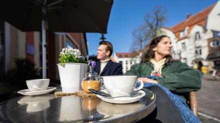08.03.2024, Nordrhein-Westfalen, Telgte: Ein junges Pärchen genießt bei strahlendem Sonnenschein eine Tasse Kaffee im Außenbereich eines Cafes.