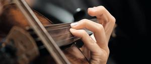 Die Hand des Mädchens auf den Saiten einer Geige in dunklen Farben