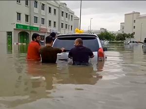 Menschen schieben auf einer überfluteten Straße in Dubai ein Auto.