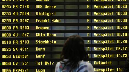 Eine Frau steht auf dem Flughafen Berlin-Schönefeld vor einer Anzeigetafel, auf der verspätete Flüge aufgelistet werden. 