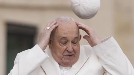 Papst Franziskus versucht am Mittwoch im Vatikan, seine Mütze aufzufangen, die der Wind weggeweht hat, als er zu seiner wöchentlichen Generalaudienz auf dem Petersplatz kommt.