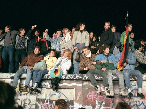 Singend und schunkelnd freuen sich junge Menschen auf der Berliner Mauer 1989 über die Grenzöffnung.