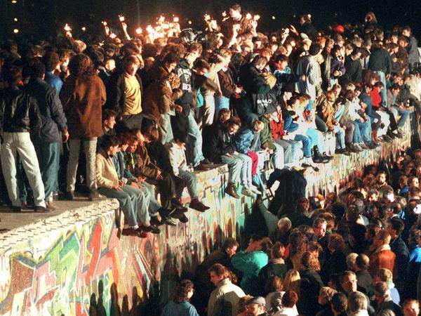 Friedliche Revolution. Jubelnde Menschen sitzen am 11. November 1989 mit Wunderkerzen auf der Berliner Mauer.