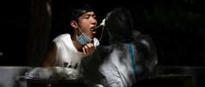  Ein Arbeiter in einem Schutzanzug nimmt bei einem Mann einen Abstrich vor, um ihn in einer Corona-Teststelle in Peking auf Covid-19 zu testen.