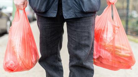 Ein Mann trägt seine Einkäufe in Plastiktüten nach Hause.