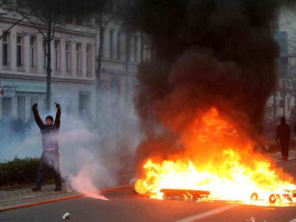 Ein Mann steht neben einer brennenden Barrikade bei Auseinandersetzungen zwischen linken Gegendemonstranten und der Polizei in Leipzig (Sachsen).