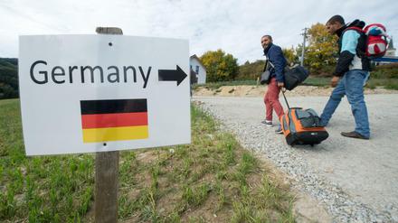Flüchtlinge aus Syrien gehen am 06.10.2015 im österreichischen Julbach nahe der deutschen Grenze an einem Schild mit der Aufschrift "Germany" und der Abbildung einer deutschen Flagge vorbei. 