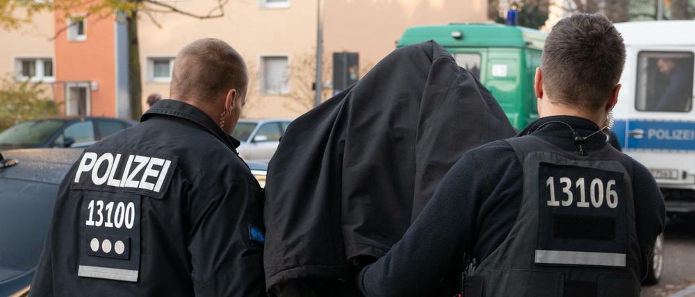 Polizeibeamte führen mit Handschellen einen festgenommenen Mann nach einer Razzia in einem Wohnhaus in Tempelhof ab. 