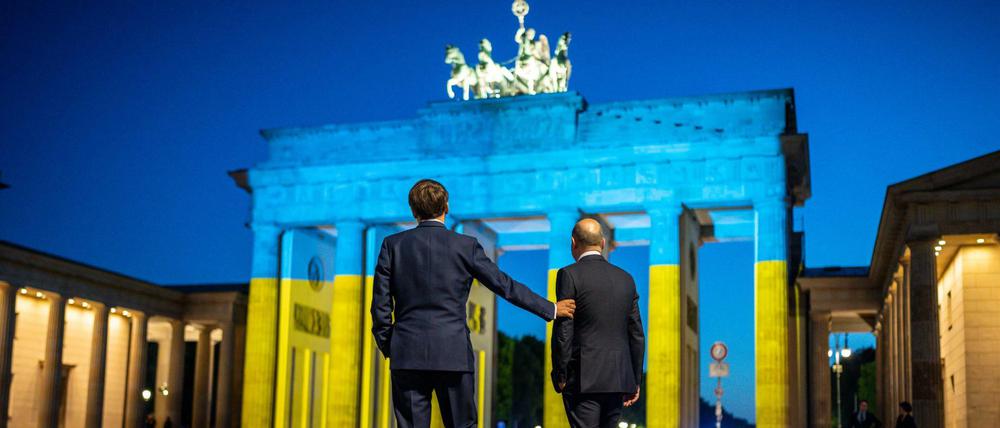 Bundeskanzler Olaf Scholz und Frankreichs Präsident Emmanuel Macron vor dem in den ukrainischen Farben beleuchteten Brandenburger Tor. A