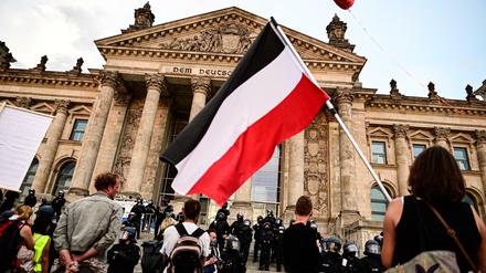 Teilnehmer einer Kundgebung gegen die Corona-Maßnahmen stehen vor dem Reichstagsgebäude - mit Reichsflagge.