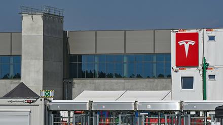 Das Logo der Firma Tesla an einem Baucontainer vor einer Halle der Autofabrik in Grünheide.