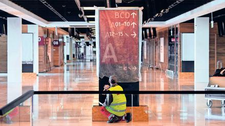 Fertig zum Putzen. Ein Arbeiter im Hauptterminal des BER reinigt ein Schild, das künftig den Weg zu den Abflugbereichen weisen soll. Der unvollendete Hauptstadtflughafen wird immer teurer.