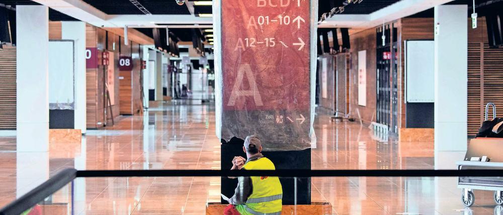 Fertig zum Putzen. Ein Arbeiter im Hauptterminal des BER reinigt ein Schild, das künftig den Weg zu den Abflugbereichen weisen soll. Der unvollendete Hauptstadtflughafen wird immer teurer.