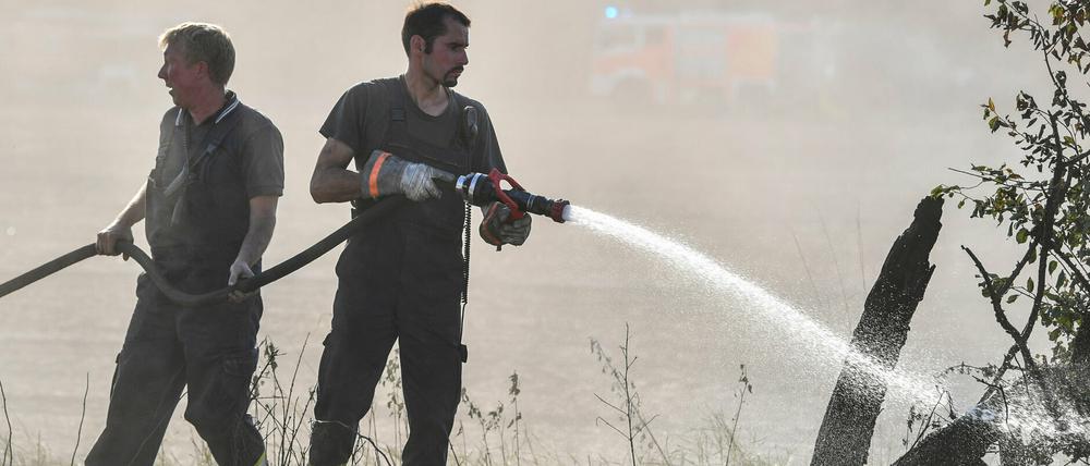 Feuerwehrmänner löschen Glutnester an einem Feldrand bei Storkow. 