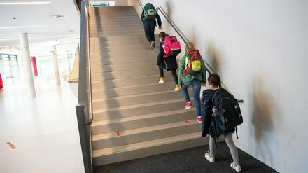 Schülerinnen und Schüler einer 4. Klasse gehen mit Abstand auf einer Treppe zu ihren Klassenräumen. 