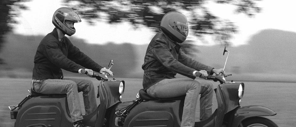 Zwei junge Männer fahren mit ihren "Schwalbe"-Rollern über einen Feldweg.