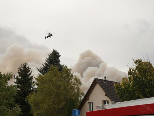 Rauch steigt neben einem Haus in Frohnsdorf auf, über dem ein Polizeihubschrauber schwebt. 
