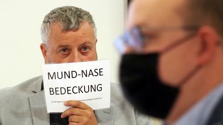 Michael Hanko (AfD) hält sich während der Landtagssitzung ein Schild mit dem Aufdruck «Mund-Nase-Bedeckung» vors Gesicht.