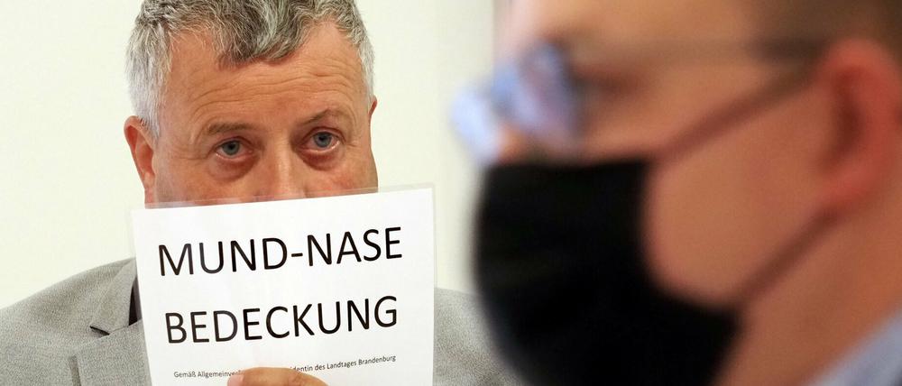 Michael Hanko (AfD) hält sich während der Landtagssitzung ein Schild mit dem Aufdruck «Mund-Nase-Bedeckung» vors Gesicht.