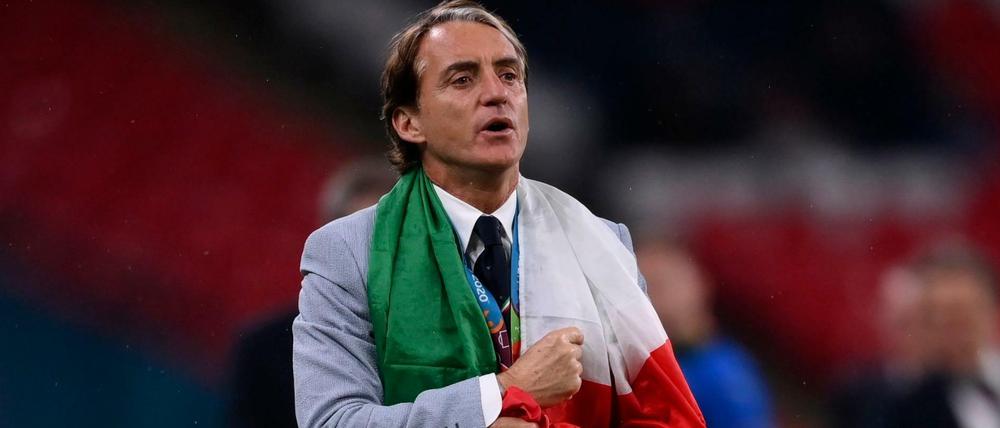Italiens Trainer Roberto Mancini geht über den Platz, eingehüllt in eine Italienflagge.