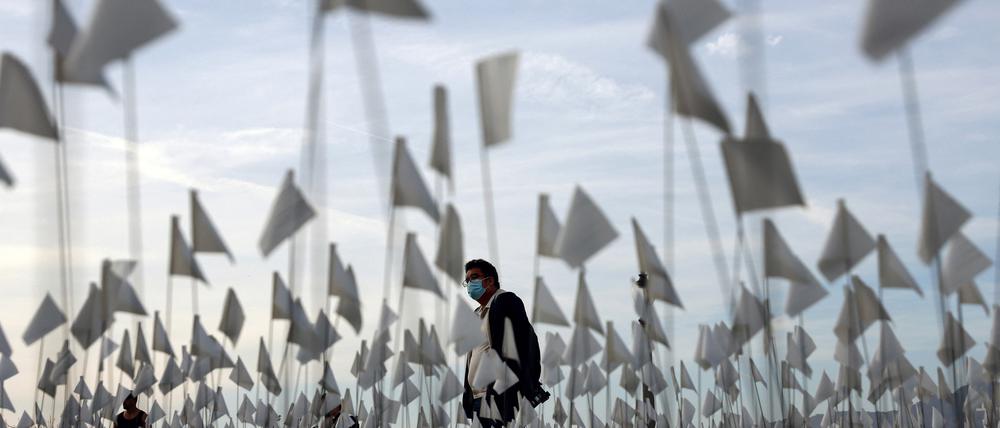LOS ANGELES, CALIFORNIA - NOVEMBER 18: A person wearing a face covering walks past a white flag memorial installation outside Griffith Observatory honoring the nearly 27,000 Los Angeles County residents who have died from COVID-19 on November 18, 2021 in Los Angeles, California. Los Angeles is holding a three-day citywide �Strength and Love� memorial honoring those who died and those who �have held the city together throughout the pandemic� including first responders and essential workers. Los Angeles County reported 26 additional deaths due to COVID-19 today.   Mario Tama/Getty Images/AFP (Photo by MARIO TAMA / GETTY IMAGES NORTH AMERICA / Getty Images via AFP)