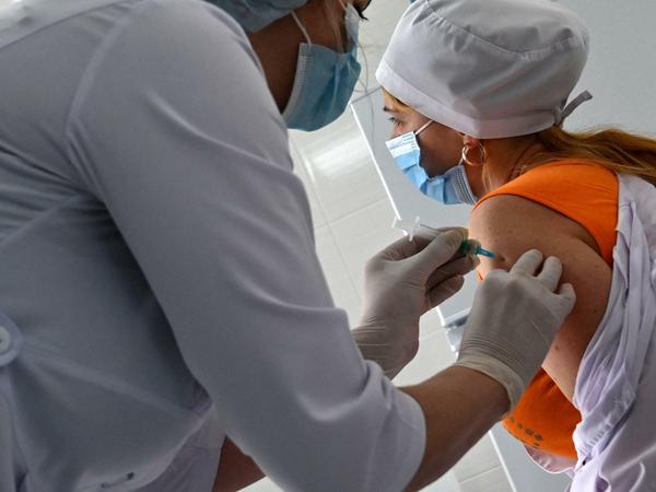 Eine Medizinerin impft eine Kollegin in den Oberarm, beide tragen weiße Kittel.