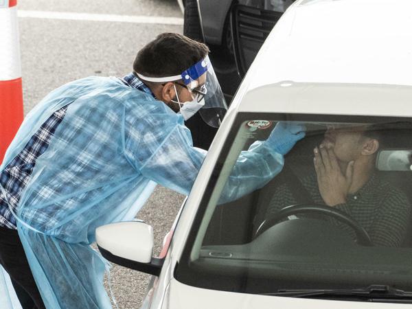 Sydney: Ein Mitarbeiter des Gesundheitswesens führt bei einem Autofahrer in einem Drive-Through-Testzentrum einen Test durch.