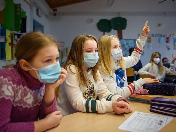 Drei Mädchen, die medizinische Gesichtsmasken tragen, sitzen nebeneinander an einem Tisch im Klassenzimmer.