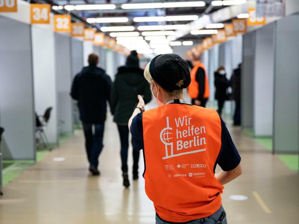 Eine Helferin in einem Berliner Impfzentrum trägt eine orange Weste mit der Aufschrift "Wir helfen Berlin".