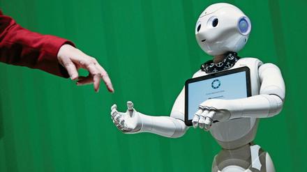 Vor einem grünen Hintergrund treffen sich eine menschliche Hand und die Hand eines Roboters.