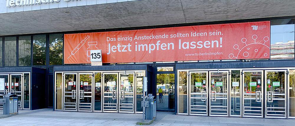 Ein rotes Banner mit der Aufschrift "Jetzt impfen lassen!" hängt über dem Eingang einer Hochschule.
