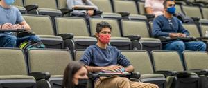 Studierende mit Mund-Nasen-Schutz sitzen mit großen Abständen voneinander in einem Hörsaal.